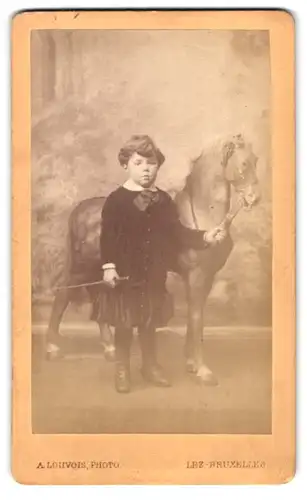 Fotografie A. Louvois, Bruxelles, 51 Chaussée de Louvain, Portrait hübsches Mädchen mit Spielzeugpferd und Reitgerte