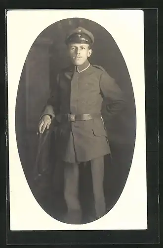AK Uniformfoto, Soldat steht an einem Stuhl mit seiner Mütze