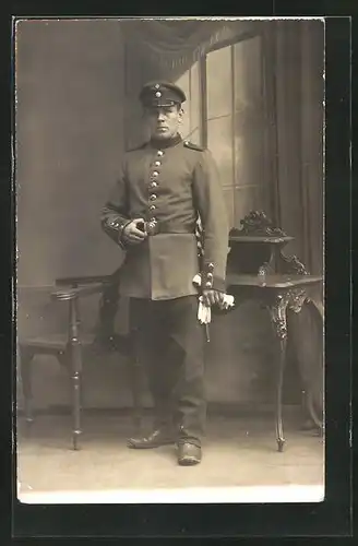 AK Uniformfoto, Soldat steht in einer Kulisse und hat die Hand an der Gürtelschnalle