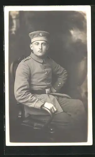 AK Uniformfoto, Soldat mit Mütze in einem Stuhl sitzend