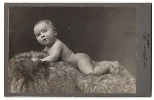 Fotografie Carl Breuer, Plettenberg i /W., Portrait nackiges Kleinkind bäuchlings auf Fell liegend