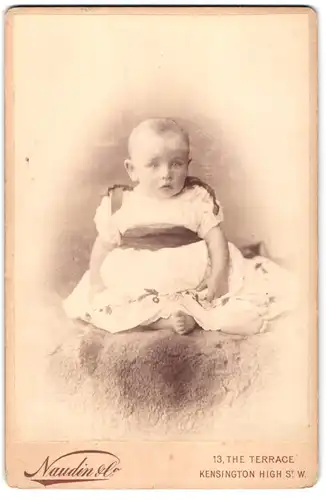 Fotografie Naudin, London-W, Kensington High St., Portrait niedliches Kleinkind im weissen Kleid mit nackigen Füssen