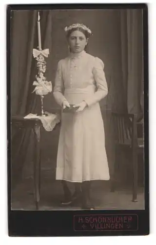 Fotografie H. Schönbucher, Villingen, Portrait Mädchen im weissen Kleid mit Blumenkranz neben Kommunionskerze