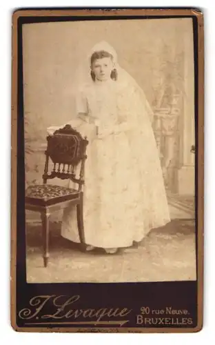 Fotografie J. Levaque, Bruxelles, 20 Rue Neuve, Portrait Mädchen im Konfirmationskleid in einer Studiokulisse
