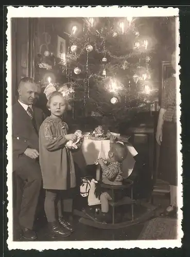 Fotografie Weihnachten - Bescherung, Knabe auf Schaukelpferd & Mädchen mit Puppe neben Weihnachtsbaum