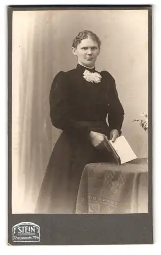 Fotografie Atelier Stein, Berlin, Chausseestr. 70 /71, Portrait hübsche Dame mit Buch in der Hand am Tisch stehend