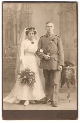 Fotografie Julius Gruschl, Neugersdorf i. S., Portrait Soldat in Uniform mit Braut, Kriegshochzeit vor Studiokulisse