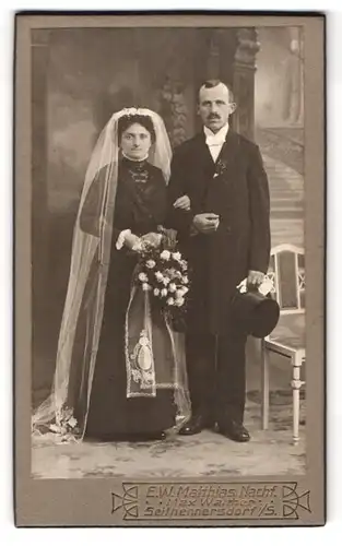 Fotografie E. W. Matthias, Seifhennersdorf i. S., Rumburgerstr., älteres Ehepaar im schwarzen Kleid mit Zylinder