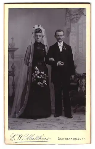 Fotografie E. W. Matthias, Seifhennersdorf, junges Ehepaar im schwarzen Kleid mit Schleier und Zylinder