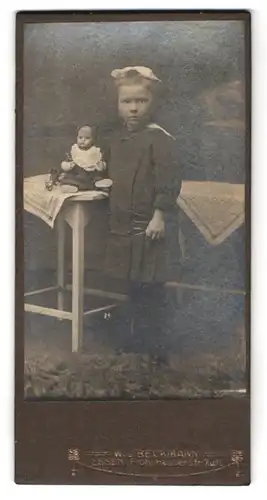 Fotografie W. J. Beckmann, Essen, Frohnhauserstr. 7-11, Portrait Mädchen im Kleid mit Puppe auf dem Tisch