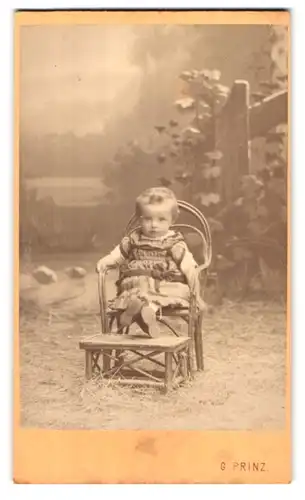 Fotografie Georg Prinz, Gossholz, Portrait Kleinkind im Kleidchen auf einem Stuhl vor Studiokulisse