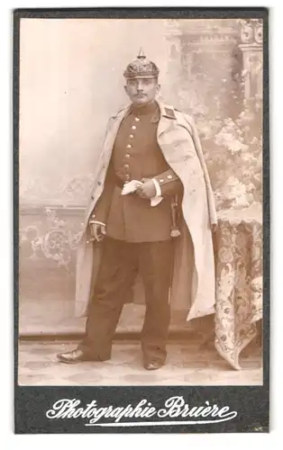 Fotografie Bruère, Mörchingen, Portrait Soldat in Uniform mit Pickelhaube und Uniformmantel, Bajonett