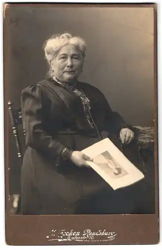 Fotografie J. Leschen, Rendsburg, Grafenstr. 10, Alte Dame sitzt ein Bild in der Hand haltend an einem Tisch