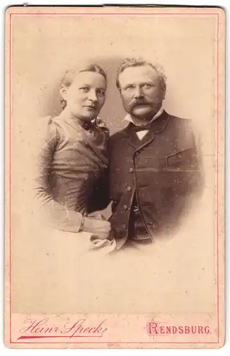 Fotografie Heinr. Speck, Rendsburg, Baronstr. 418, Herr mit Oberlippenbart und Dame mit gemustertem Kleid Arm in Arm