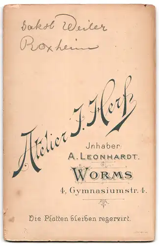 Fotografie Atelier J. Herf, Worms, Gymnasiumstr. 4, Kleiner Bursche in schwarzem Anzug mit Hut neben Kummunionskerze