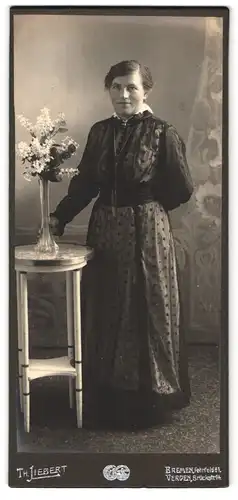Fotografie Th. Liebert, Bremen, Fehrfeld 81, Portrait charmant blickende Dame im bestickten Kleid am Tisch stehend