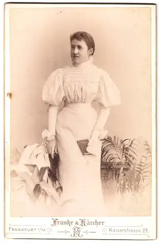 Fotografie Franke & Kärcher, Frankfurt a/M., Kaiserstrasse 29, Portrait Frau in langem, weissem Kleid mit Büchlein