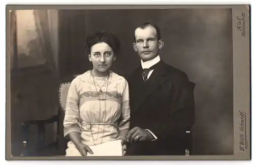 Fotografie f. Wilh. Schmidt, Kiel, Holstenstr. 22, Herr mit Krawatte und junge Dame in besticktem Kleid