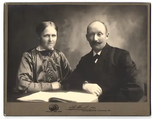 Fotografie A. Fuul, Flensburg, Grossestr. 35, Herr mit Schnauzbart und Dame mit Zierkragen sitzen an Tisch