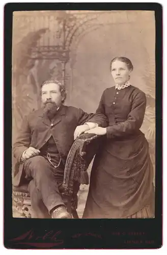 Fotografie Nille, Lincoln, Nebraska, O Street 1029, Sitzender Herr mit Oberlippen- und Kinnbart und Frau mit Zierkragen