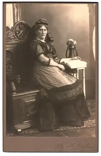 Fotografie Fr. Becker, Höftgrube, Dame mit geflochtenen Haaren sitzt auf beschnitzter Bank und liest ein Buch