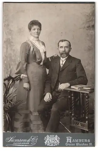 Fotografie Samson & Co., Hamburg, Grosse Bleichen 31, Sitzender Mann mit Vollbart mit Frau in geschmücktem Kleid