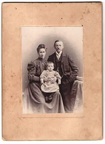 Fotografie Oskar Dubienski, Wien, Mann mit Schnauzbart und Frau in gestreiftem Kleid mit Kleinkind in kariertem Kleid
