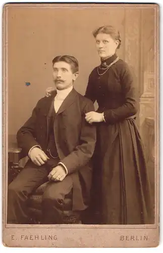 Fotografie E. Faehling, Berlin, Sitzender Mann mit Mittelscheitel und Schnauzbart mit Frau mit vierreihiger Kette