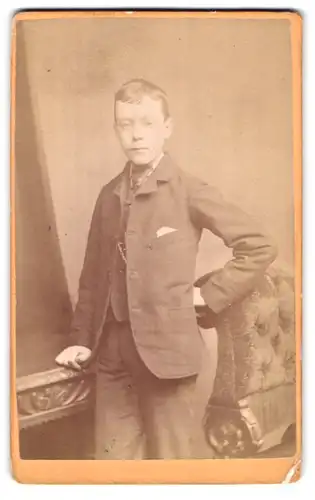 Fotografie William Lacey, London, 20 Blackfriars Road, Portrait niedlicher Bube im Anzug am Tisch stehend
