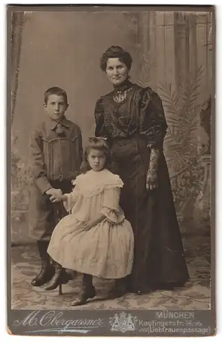 Fotografie M. Obergassner, München, Kaufingerstr. 14, Mutter in schwarzem Kleid mit ihren beiden Kindern
