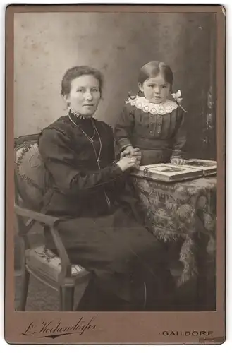 Fotografie L. Kochendörfer, Gaildorf, Portrait stolze Mutter mit niedlicher Tochter und Buch am Tisch sitzend