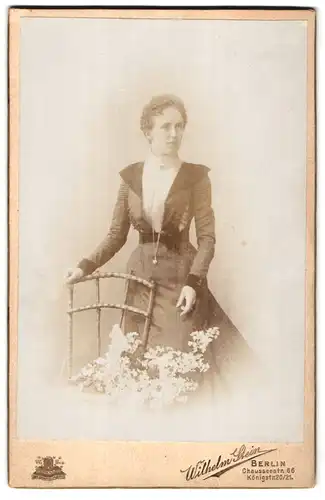 Fotografie Wilhelm Stein, Berlin, Chausseestr. 66, Portrait elegant gekleidete Dame steht an einem Stuhl