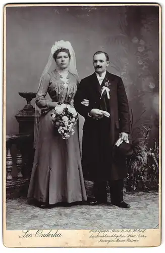 Fotografie Leo. Onderka, Gmünd, Portrait junges Paar in Hochzeitskleidung mit Schleier und Blumenstrauss