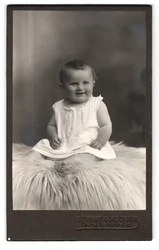Fotografie Lienhard & Salzborn, Chur, Portrait bezaubernd lächelndes kleines Mädchen auf Fell sitzend
