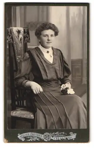 Fotografie C. Güttges, Zittau i. S., Bahnhofstr. 27, Portrait einer elegant gekleideten Dame mit Rosen in der Hand