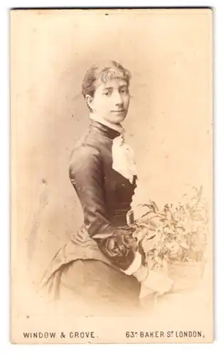 Fotografie Window & Grove, London, 63a Baker St., Portrait hübsches Fräulein steht an einer Blumenschale