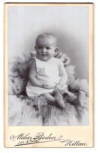 Fotografie Atelier Boden, Zittau i. S., Juststr. 2, Portrait süsses Kleinkind im weissen Hemdchen auf Fell sitzend