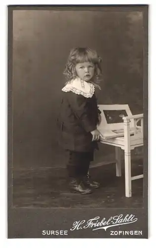 Fotografie H. Kriebel-Sahli, Zofingen, Luzernerstr., Portrait süsses kleines Mädchen mit Buch am Stuhl stehend