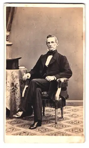Fotografie C.J. Malmberg, Stockholm, Dronninggatan 42, Portrait Herr im eleganten Anzug, Zylinder auf Beistelltisch