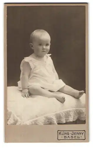 Fotografie Kling Jenny, Basel, Portrait süsses Kleinkind im weissen Kleidchen auf einem Kissen sitzend
