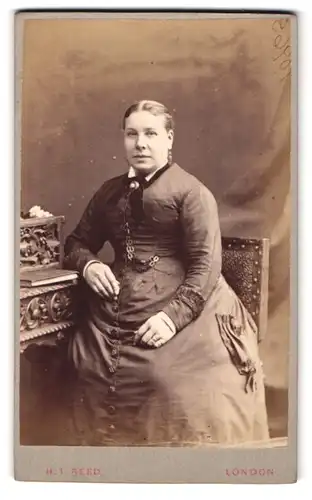 Fotografie H. T. Reed, London, 16 Tottenham Court Road, Portrait einer elegant gekleideten Frau am Tisch sitzend