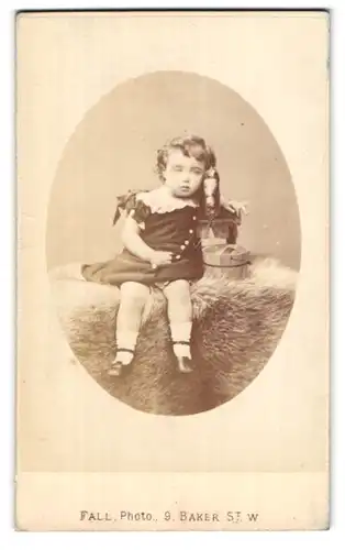 Fotografie T. Fall, London-W, 9 Baker Street, Portman Square, Portrait kleines Mädchen im Kleid mit Spielzeugpferd