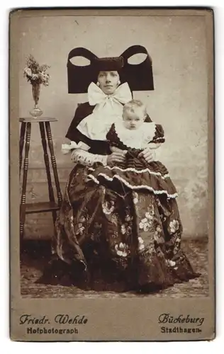 Fotografie Friedr. Wehde, Bückeburg, Portrait Mutter in Tracht mit Kind auf dem Schoss