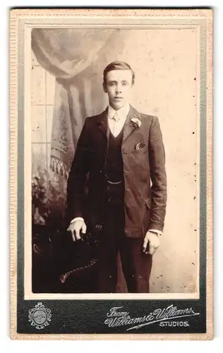 Fotografie Williams & Williams, Cardiff, Junger Mann im dunklen Anzug mit Blumen am Revers
