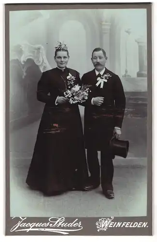 Fotografie Jacques Studer, Weinfelden, Hochzeitspaar vor Studiokulisse in schwarz gekleidet, Bräutigam mit Zylinder