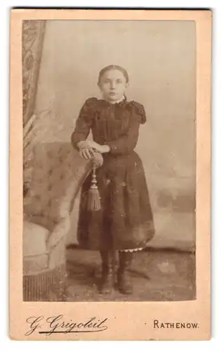 Fotografie G. Grigoleit, Rathenow, Berlinerstr. 11, Portrait süsses Mädchen im Kleidchem am Sessel stehend