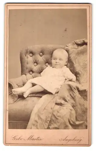Fotografie Gebr. Martin, Augsburg, Bahnhofstr., Portrait Kleinkind im weissen Hemdchen im Sessel lehnend