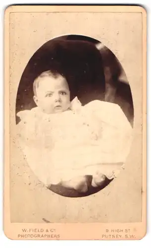 Fotografie W. Field & Co., Putney-SW, 9, High St., Portrait süsses Baby im weissen Kleid mit nackigen Füssen
