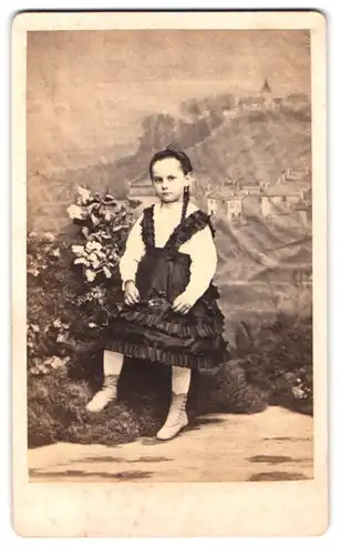 Fotografie L. Parey, St. Menehould, Portrait kleines Mädchen im schwarzen Kleid mit Zopf vor einer Studiokulisse