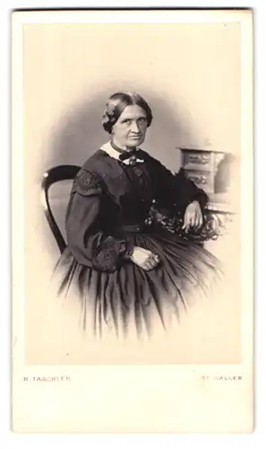 Fotografie B. Täschler, St. Gallen, Portrait alte Frau im schwarzen Kleid mit Zöpfen sitzt am Sekretär
